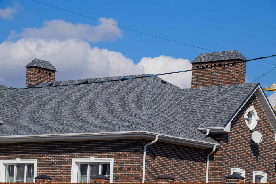 Close up view of a brick home with dark gray asphalt shingles