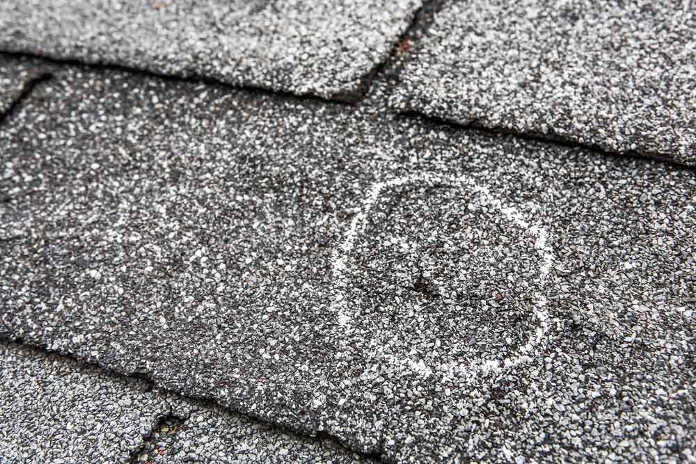 Small hole in an asphalt roofing shingle with a white chalk circle around it