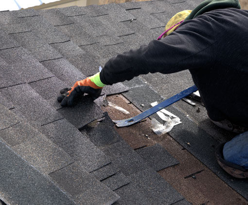 Close up of a roofer using a pry bar to lift loose asphalt shingles